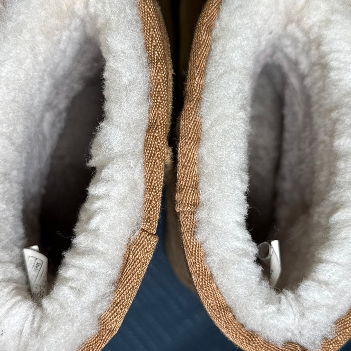 Close-up of cream-colored plush lining and interior tags in chestnut Koolaburra by UGG boots.