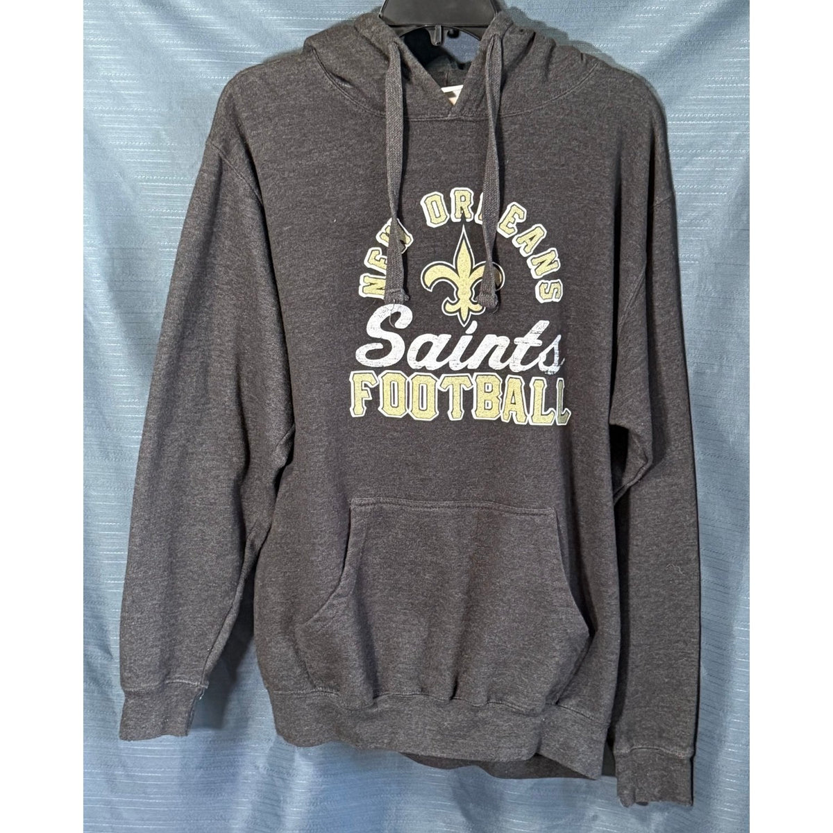 Front view of Majestic men's large charcoal gray New Orleans Saints football hoodie with gold fleur-de-lis graphic, white Saints lettering and kangaroo pocket.