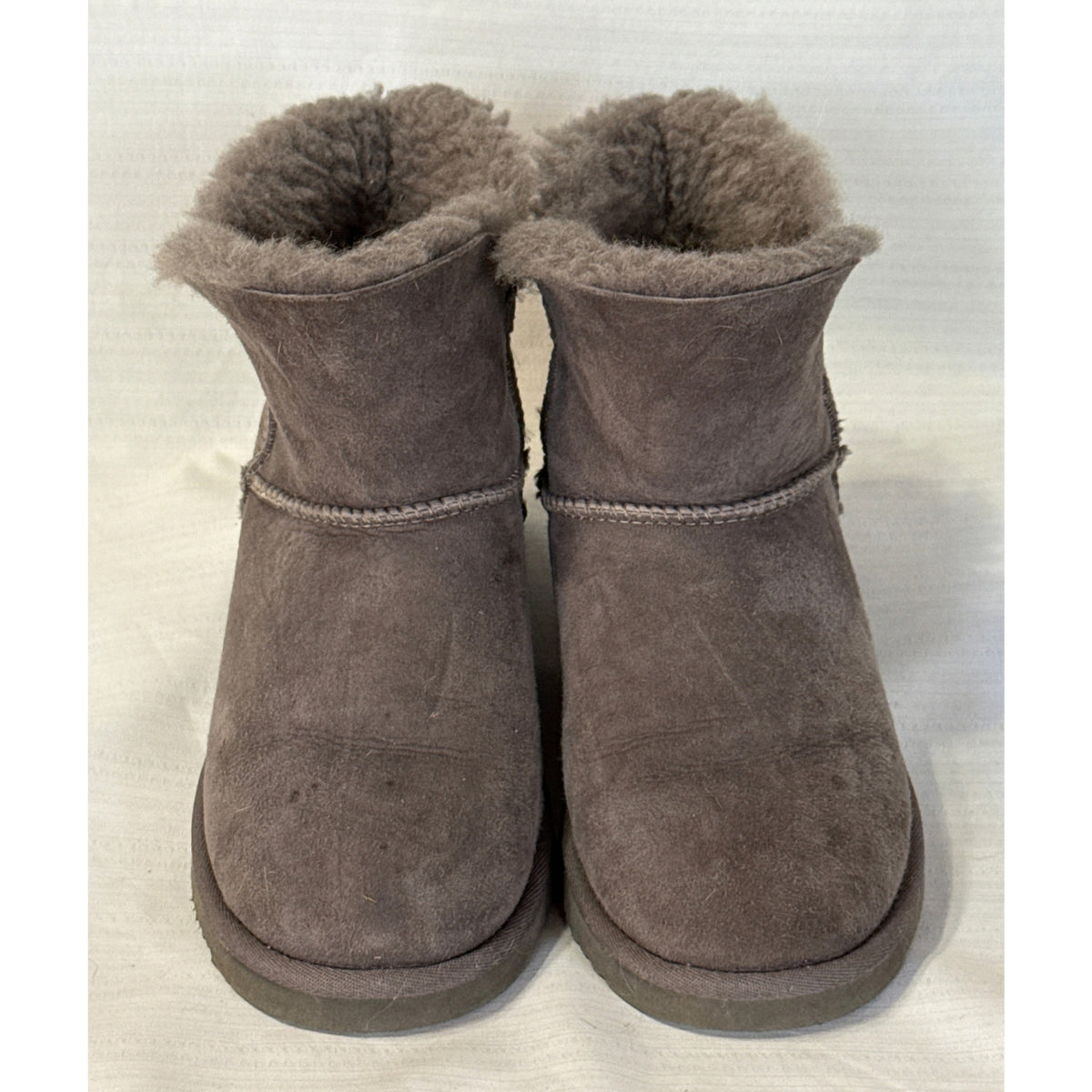 Front view of Member's Mark gray sheepskin boots showing rounded toes, short shafts, fluffy lining, and suede surface wear.