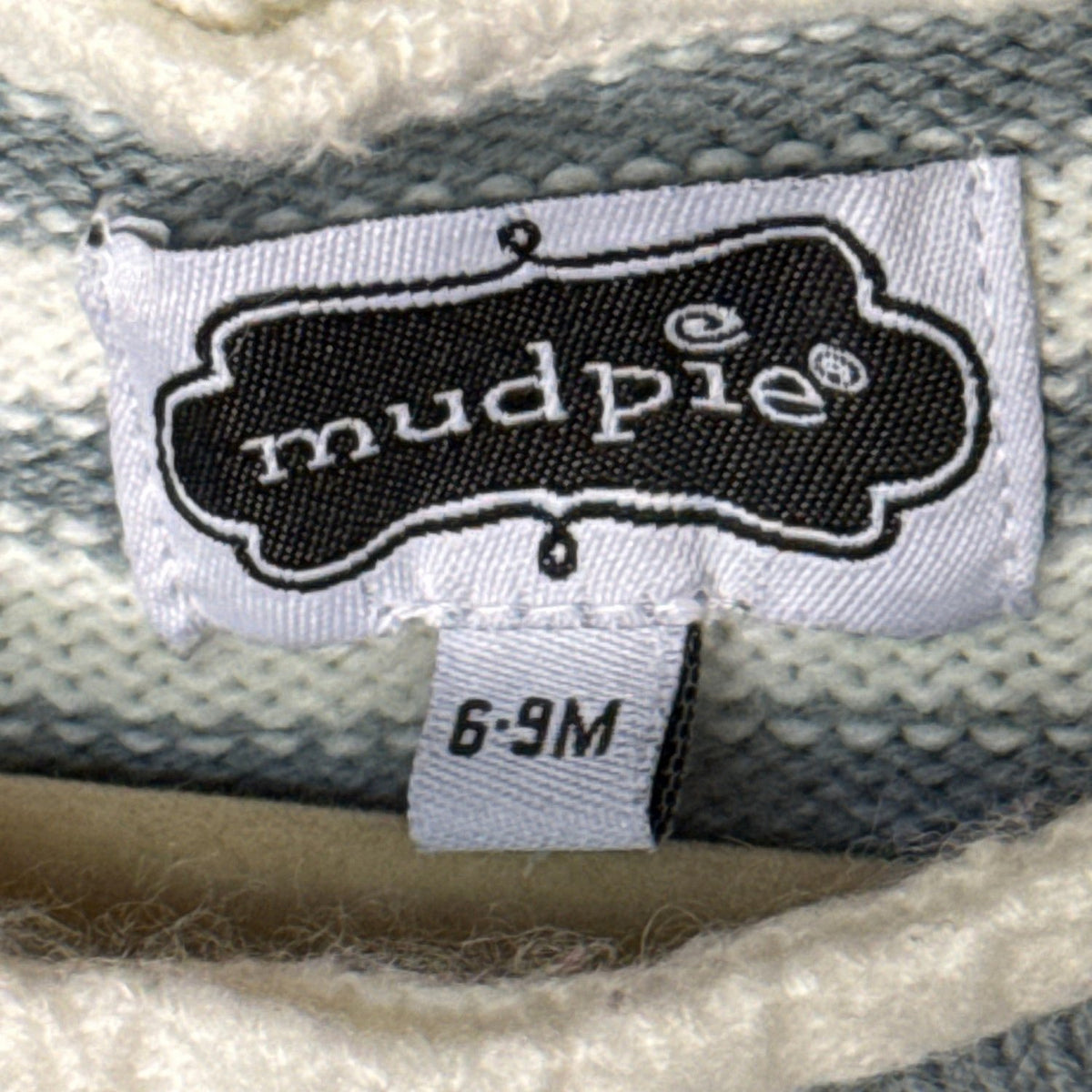 Mud Pie baby clothing label showing size 6–9 months on striped knit fabric.