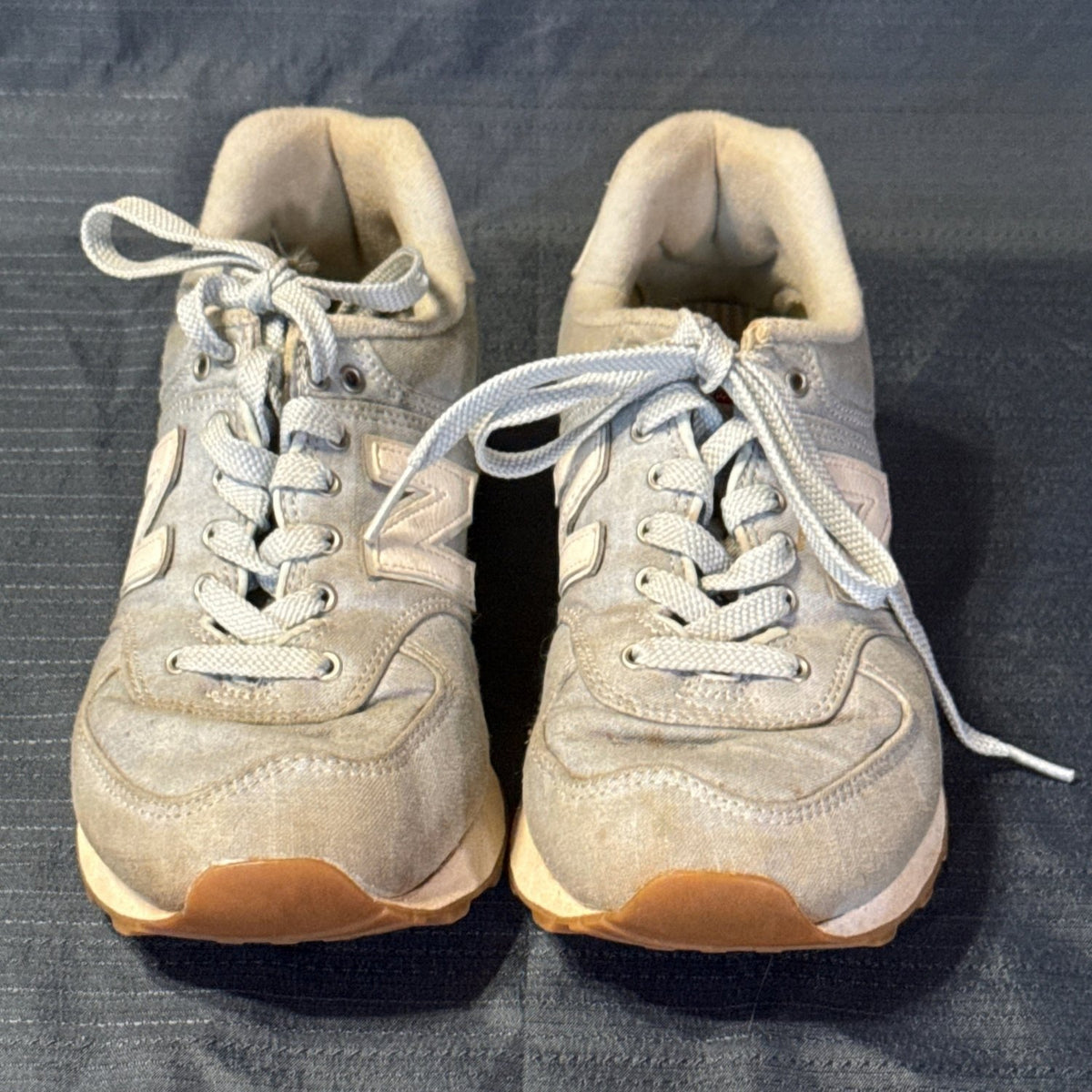 Front view of light blue New Balance 574 lace-up sneakers showing rounded toes and visible discoloration.