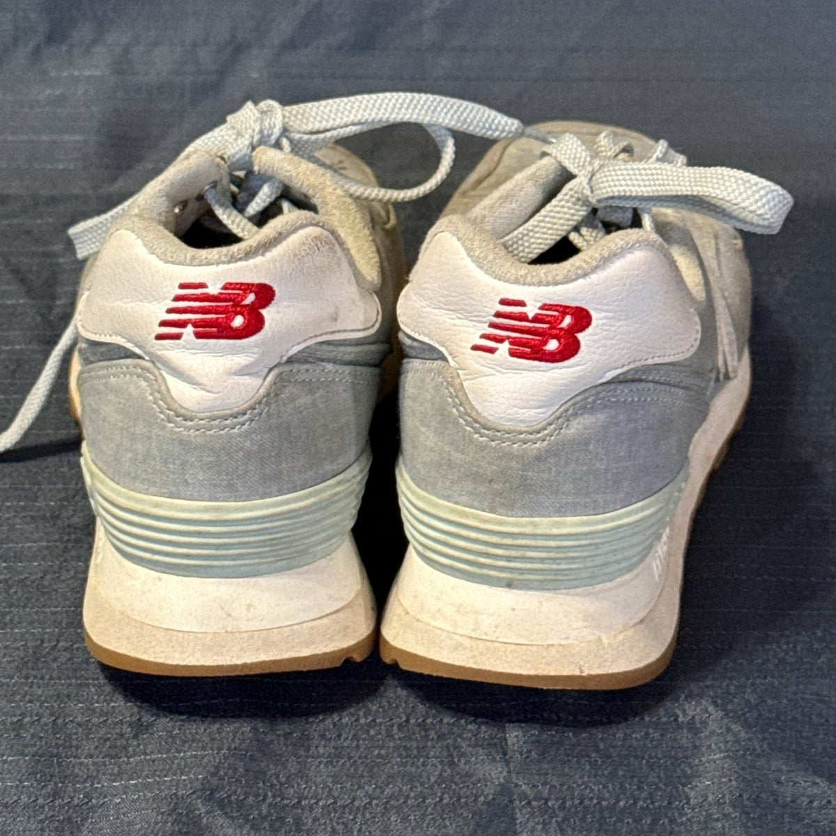 Back view of New Balance 574 sneakers showing white heel panels with red embroidered logos.