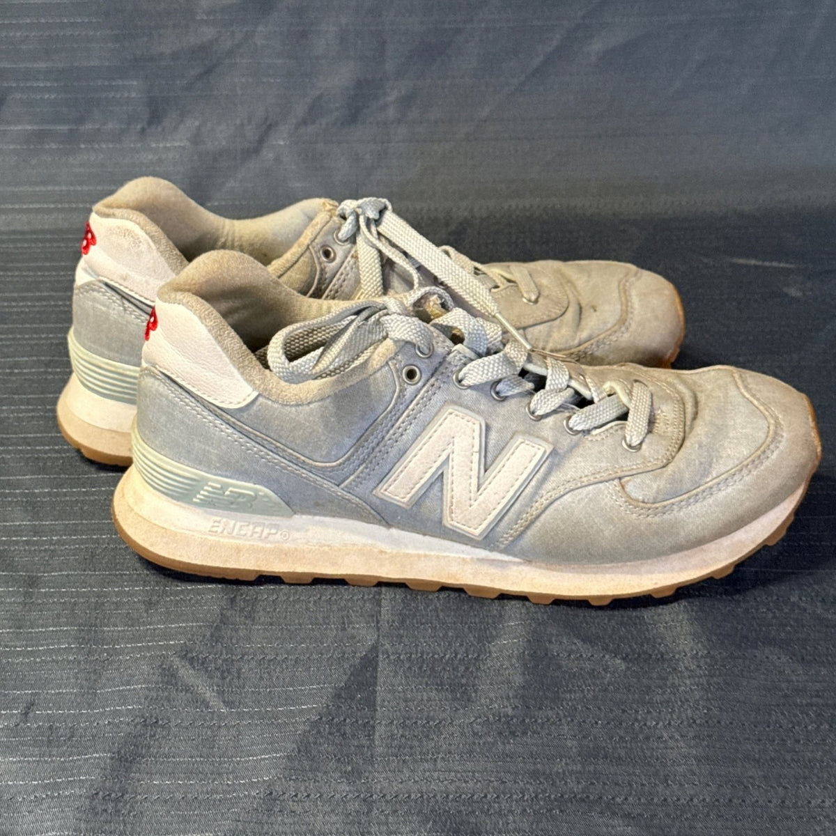 Right-side view of New Balance 574 sneakers showing woven uppers, white midsoles, and visible wear.