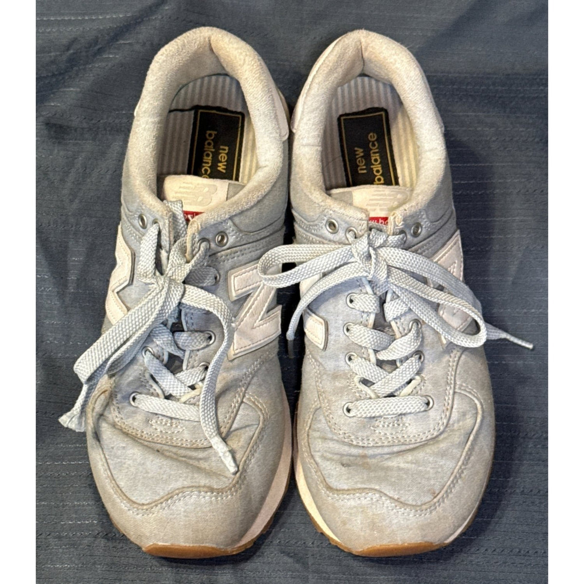 Top view of New Balance 574 sneakers showing blue laces, padded collars, insoles, and discoloration.
