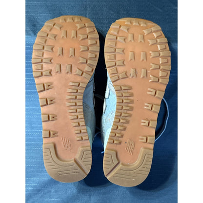 Bottom view of both New Balance 574 sneakers showing tan outsoles and remaining tread.