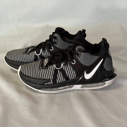 Side view of black and white Nike LeBron Witness 7 basketball sneakers with white Swoosh and visible heel cushioning.