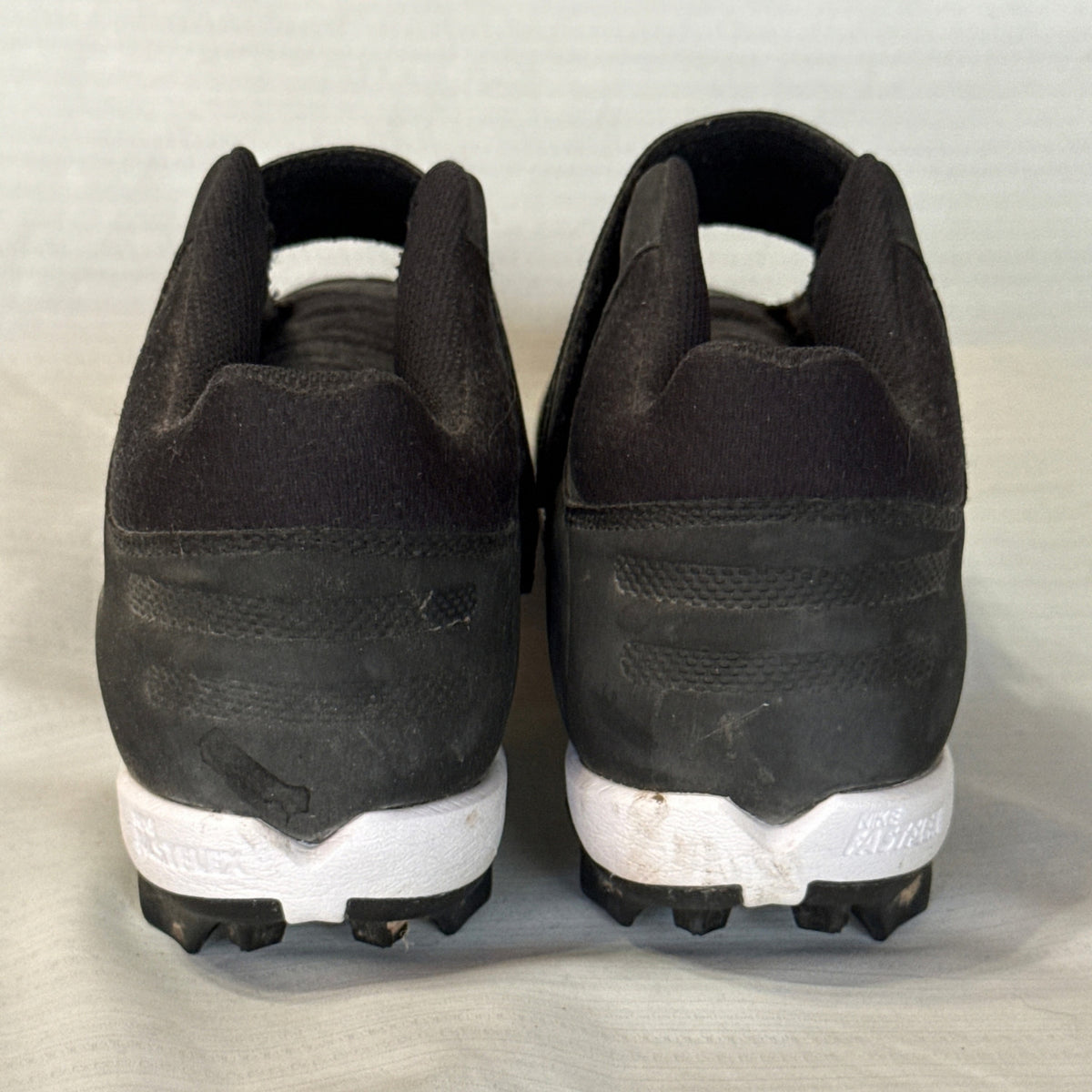 Back view of Nike baseball cleats showing black heels, white midsoles, and normal surface wear.