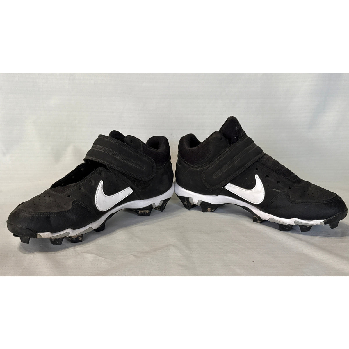 Inner side views of black and white Nike baseball cleats with ankle straps and missing shoelaces.