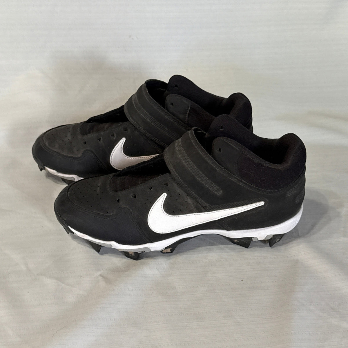 Left-facing angled view of black Nike baseball cleats with white Swooshes and adjustable ankle straps.