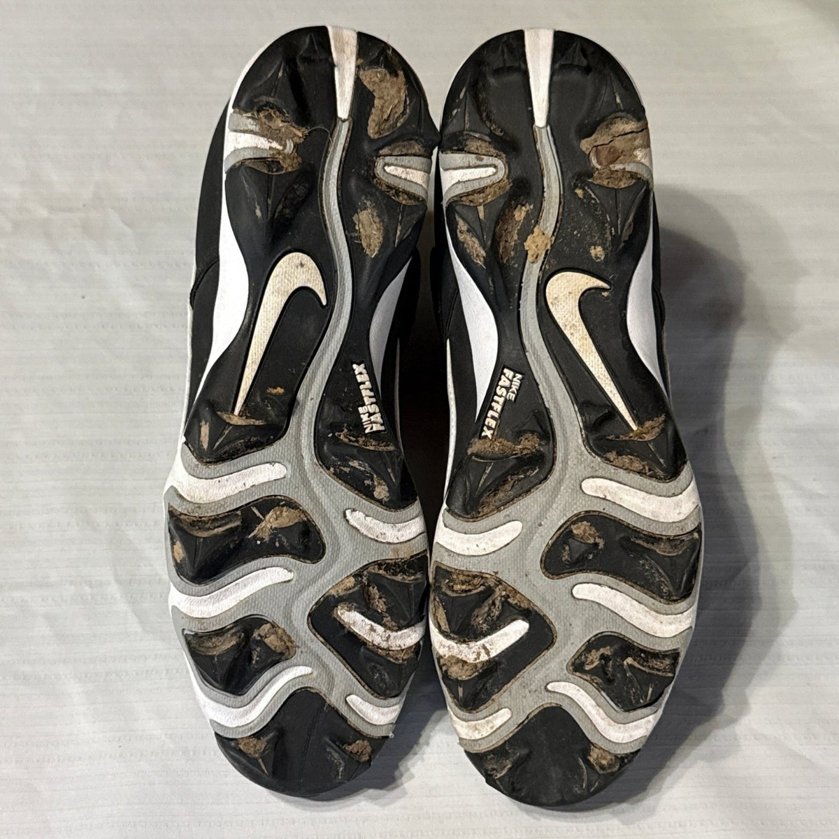 Bottom view of both Nike baseball cleats showing molded studs, Nike Fast Flex branding, and dirt around the soles.