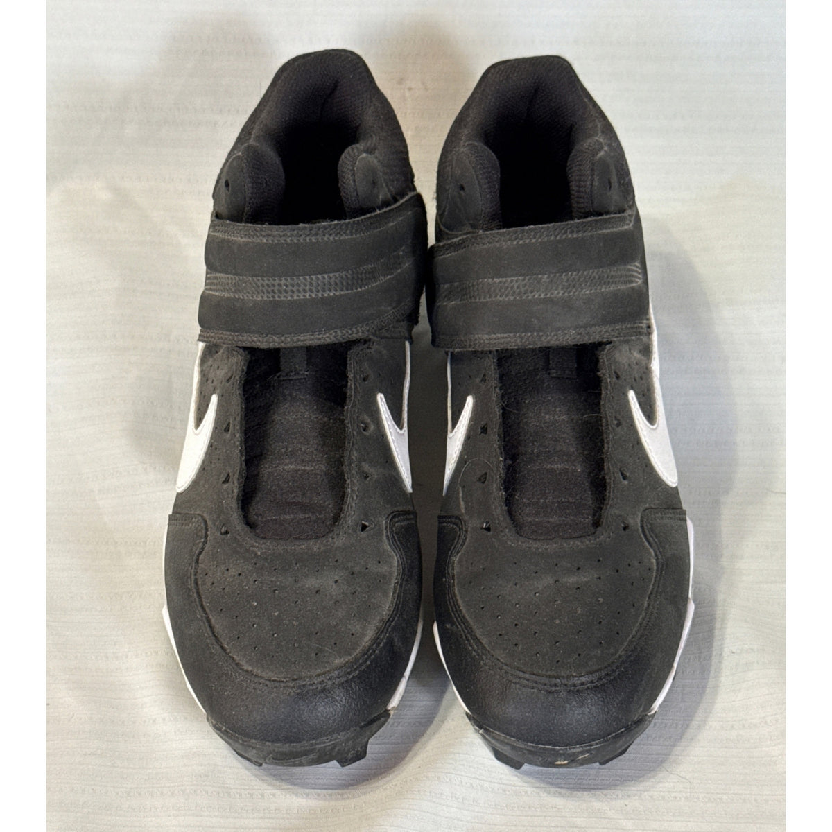 Front view of black Nike baseball cleats showing perforated toes, ankle straps, and missing shoelaces.