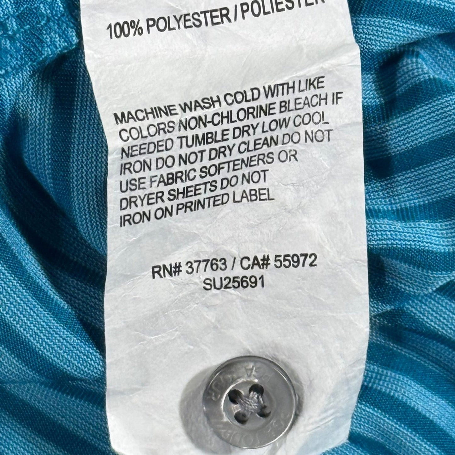 Care tag showing 100% polyester fabric and attached replacement button on PGA TOUR polo.