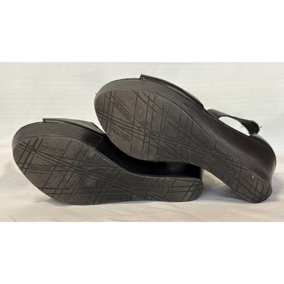 Bottom soles of black Reaction Kenneth Cole Sole Kick wedge sandals showing tread and wear.
