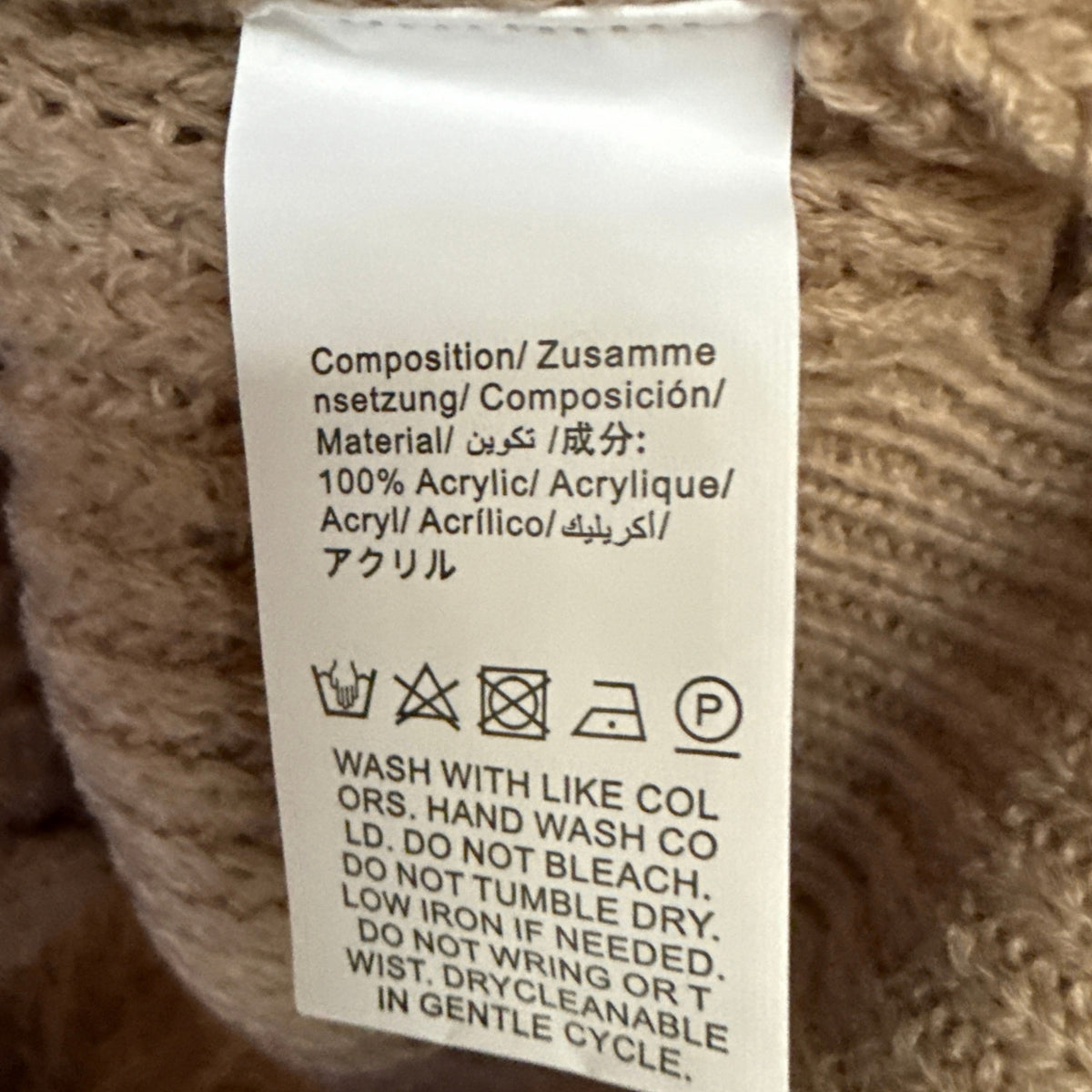 Material and care label on a beige SHEIN sweater showing 100% acrylic and hand wash cold instructions.
