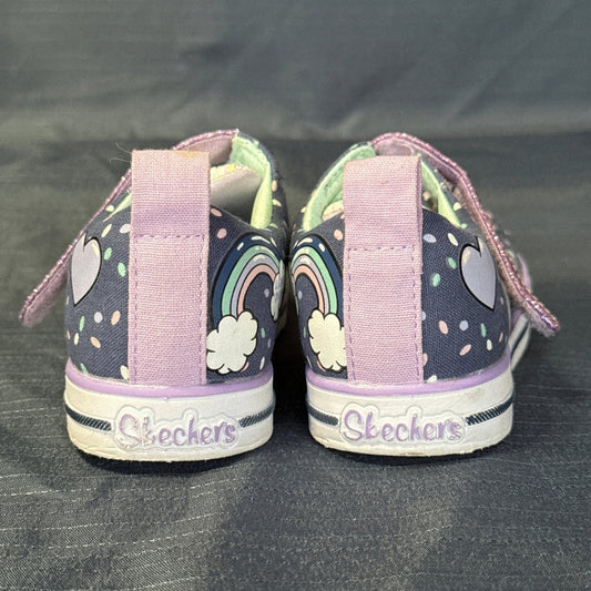 Back view of Skechers Twinkle Toes sneakers with purple pull tabs, rainbow graphics, and Skechers heel branding.

