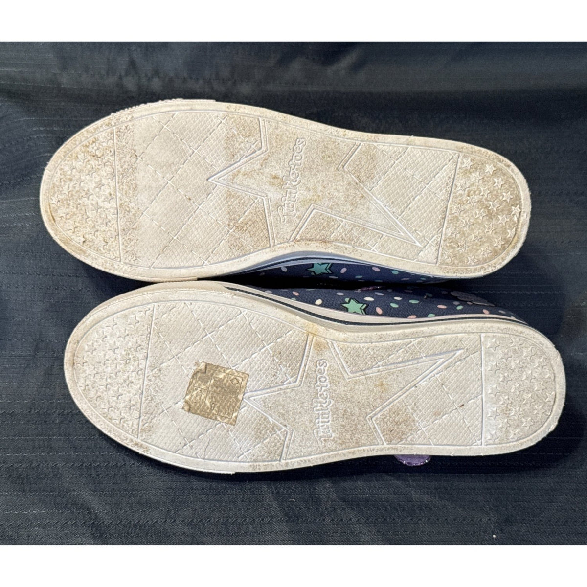 Bottom view of Skechers Twinkle Toes sneakers showing star-patterned tread and discoloration on the soles.
