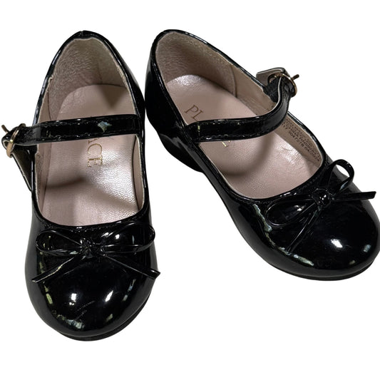 Pair of black patent leather shoes with a bow on a white background