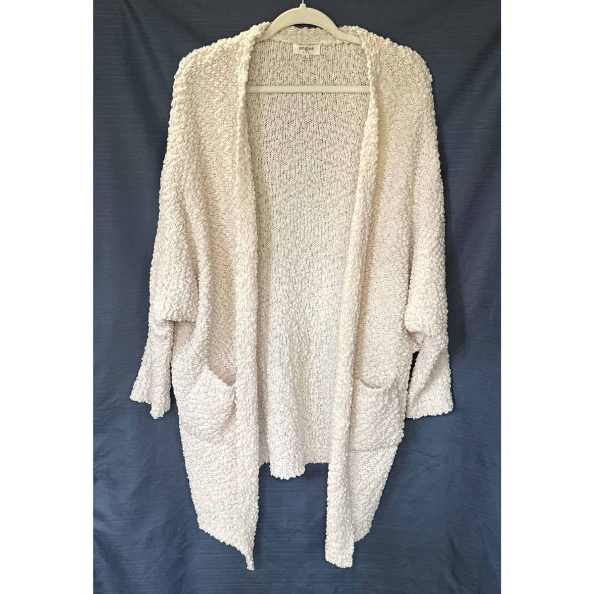 Front view of a cream Umgee women’s medium popcorn knit cardigan with a draped open front, two pockets, and longer front points.