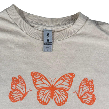 Gildan Heavy Cotton neck tag on a women's medium tan butterfly graphic t-shirt.