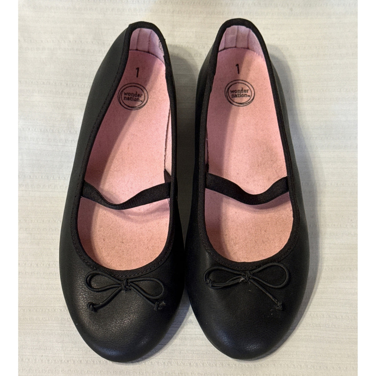 Front view of girls’ black Wonder Nation ballet flats showing decorative bows, rounded toes, and pink insoles.