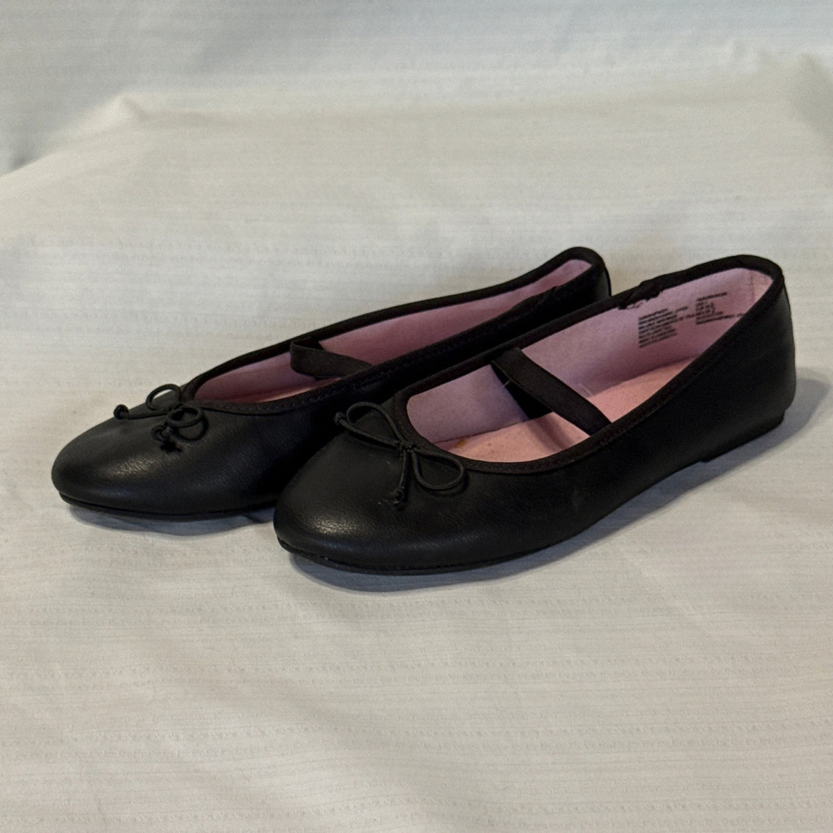 Left angled view of Wonder Nation black bow ballet flats showing rounded toes and flat soles.
