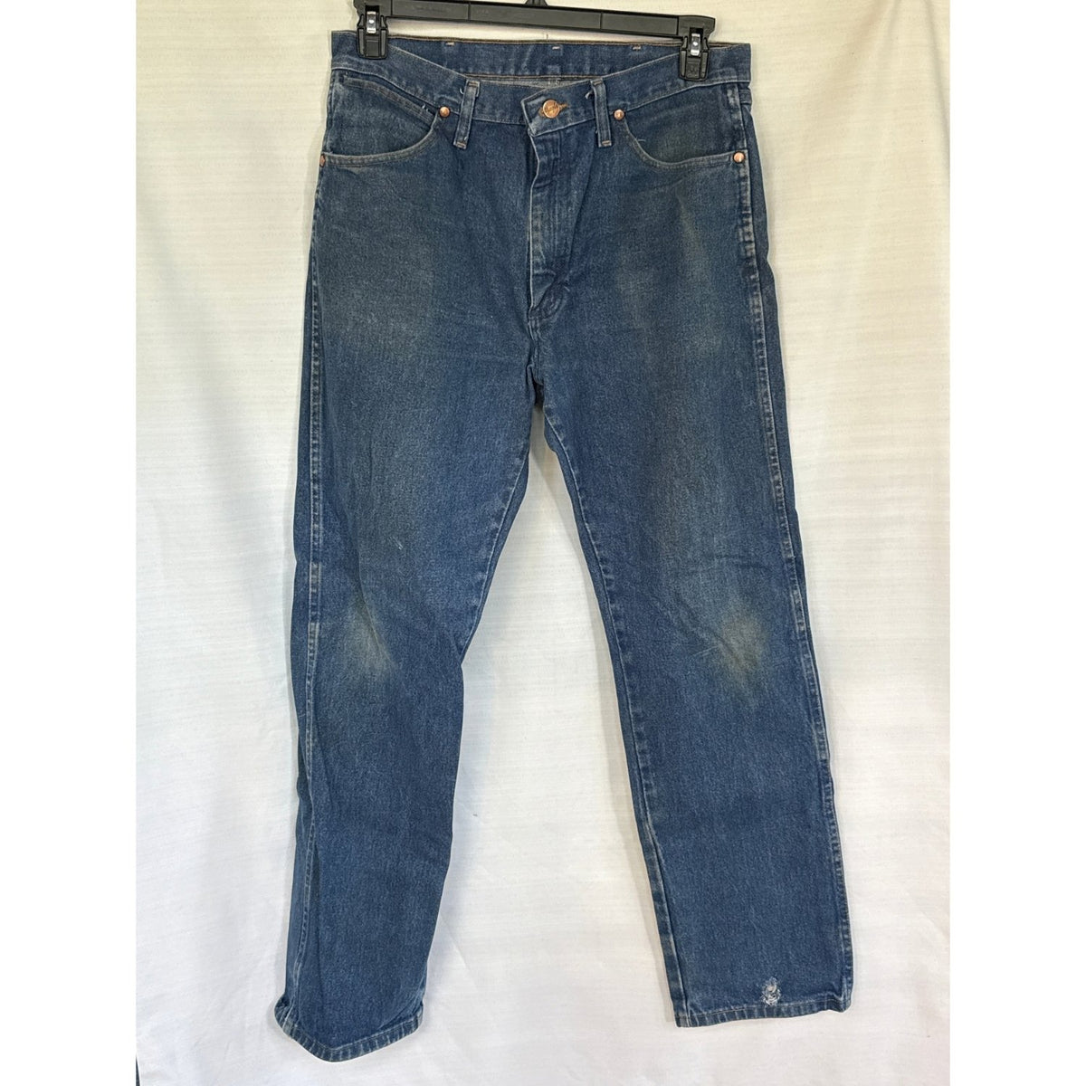 Front of Wrangler 13MWZ men’s 34×32 medium-blue Cowboy Cut jeans showing fading, knee stains, and a small hole near the left leg hem