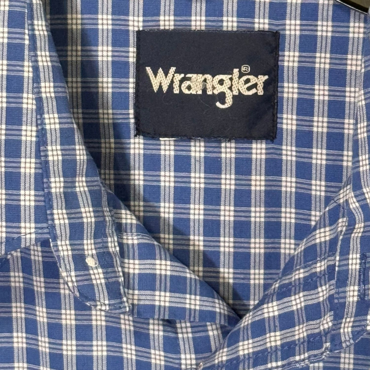 Close-up of Wrangler brand label and blue and white plaid fabric inside men's Western pearl snap shirt.